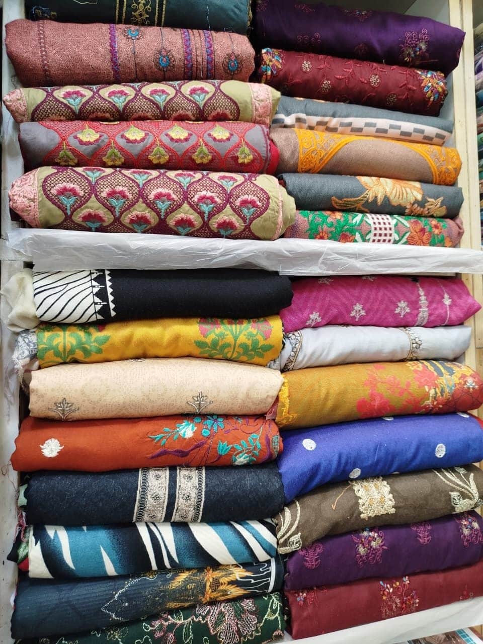 Stacks of embroidered winter suits in maroon, mustard, navy and purple at Shahzad Cloth House